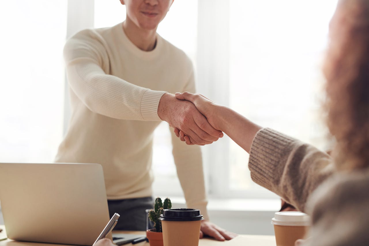 heros-img Close-up of professionals shaking hands over coffee in a modern office.